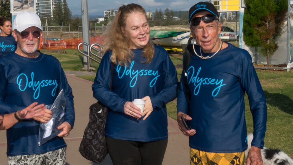965 World Champion Felipe Pomar and his wife Christina walking at Kirra, wearing matching blue "Odyssey" long-sleeve surf shirts.